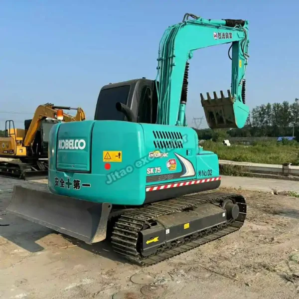 Rear view of the Kobelco SK75 featuring its standard dozer blade for grading.